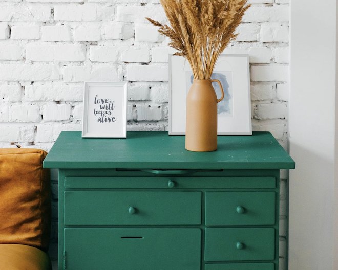 a vase of leaves on top of a chest of drawers